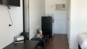 Une petite pièce propre, avec un lit, un bureau, une chaise, un téléviseur fixé au mur et une fenêtre.