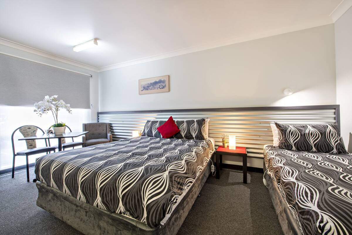 A hotel room with a large bed, two bedside tables, a chair, a small table with a plant, and a picture on the wall.