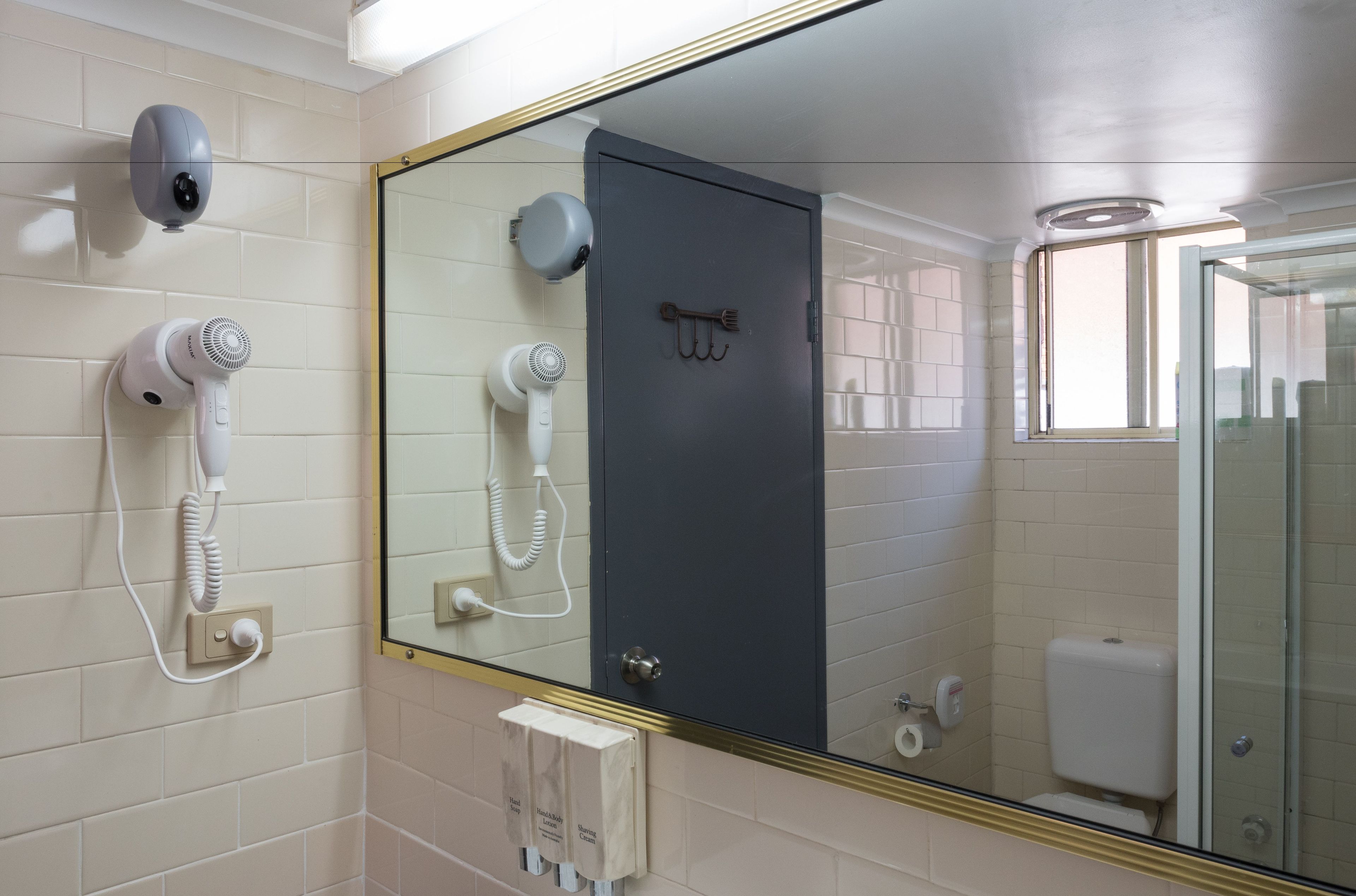 A bathroom with a large mirror, two hair dryers mounted on the wall, a toilet, and a glass shower enclosure.