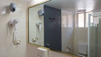 A bathroom with a large mirror, two hair dryers mounted on the wall, a toilet, and a glass shower enclosure.