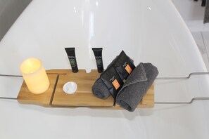 A wooden tray with a candle, two tubes of lotion, a towel, and a small container on a white surface.