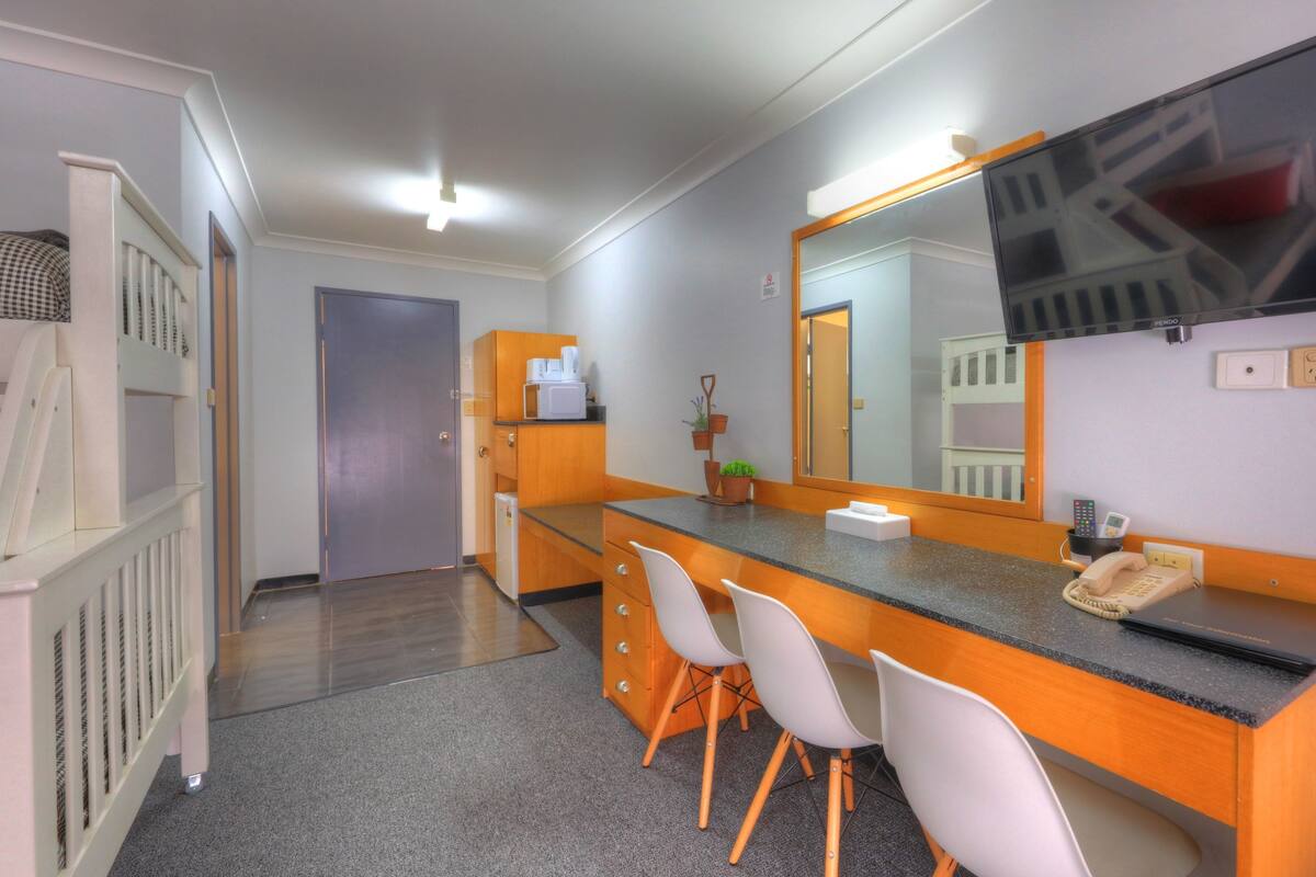 A hotel room with a kitchenette, a large mirror, a flat-screen TV, and a desk with chairs.