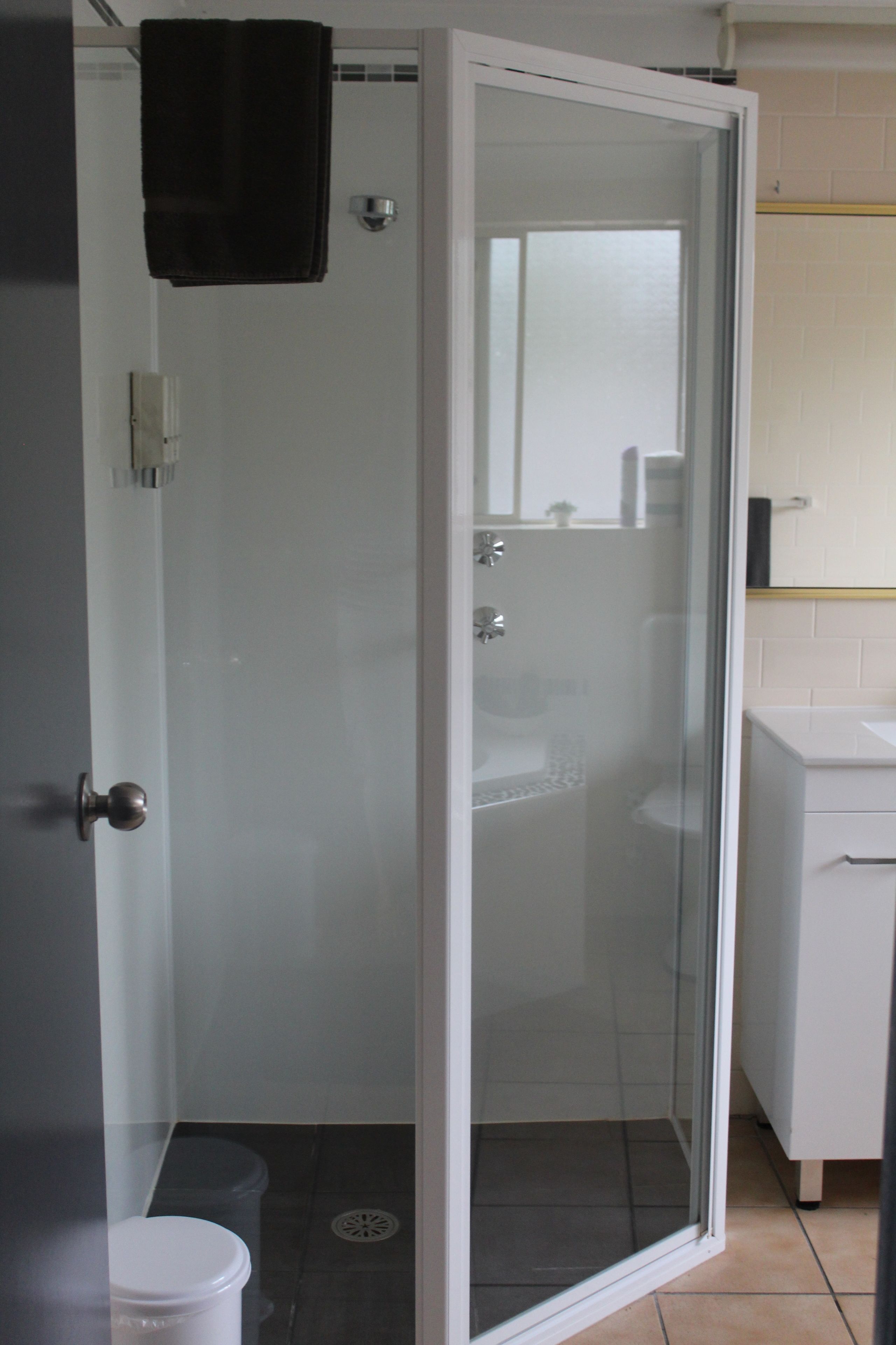 Un baño con ducha separada por vidrio, un lavamanos blanco y un inodoro.