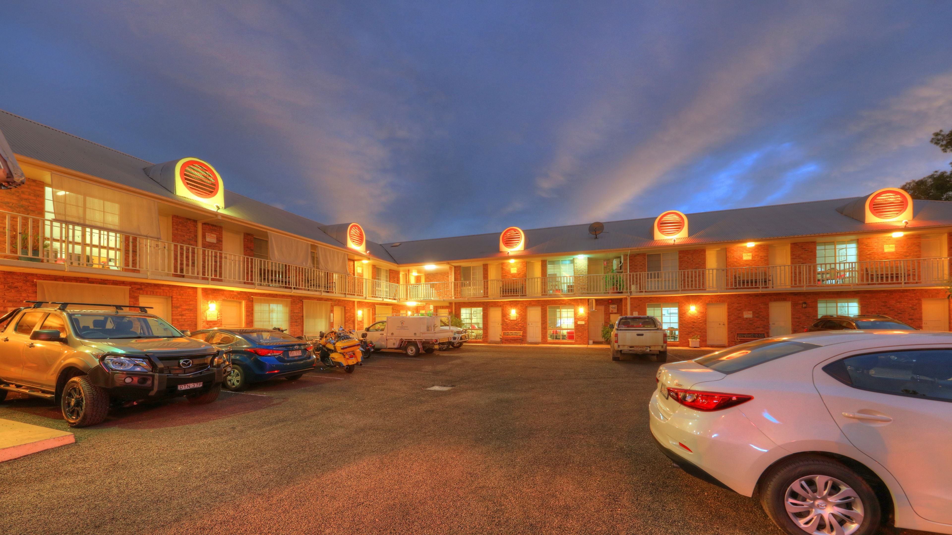 Un motel de dos pisos, con estacionamiento y cielo despejado.