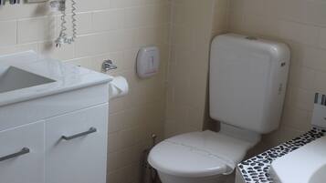 Un baño con inodoro, lavamanos y secador de pelo en la pared.