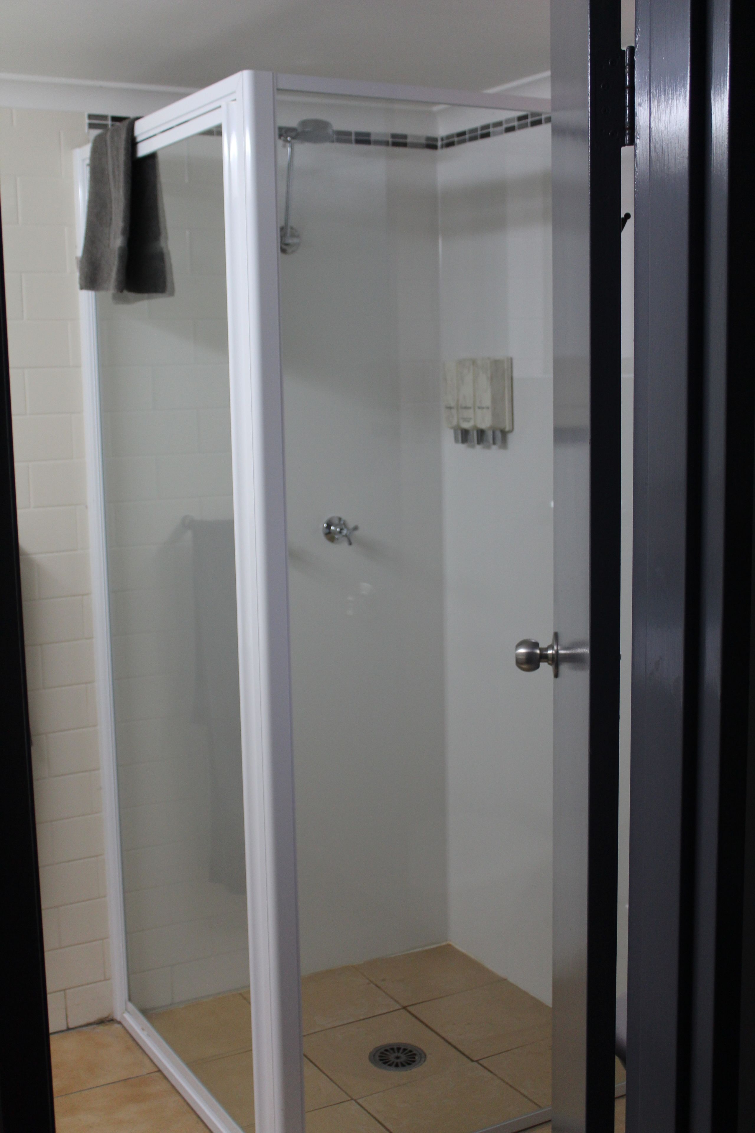 A glass-enclosed shower area with a white tiled floor and a towel hanging on the door.