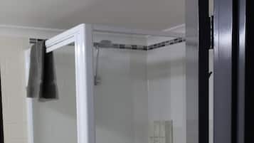 A glass-enclosed shower area with a white tiled floor and a towel hanging on the door.