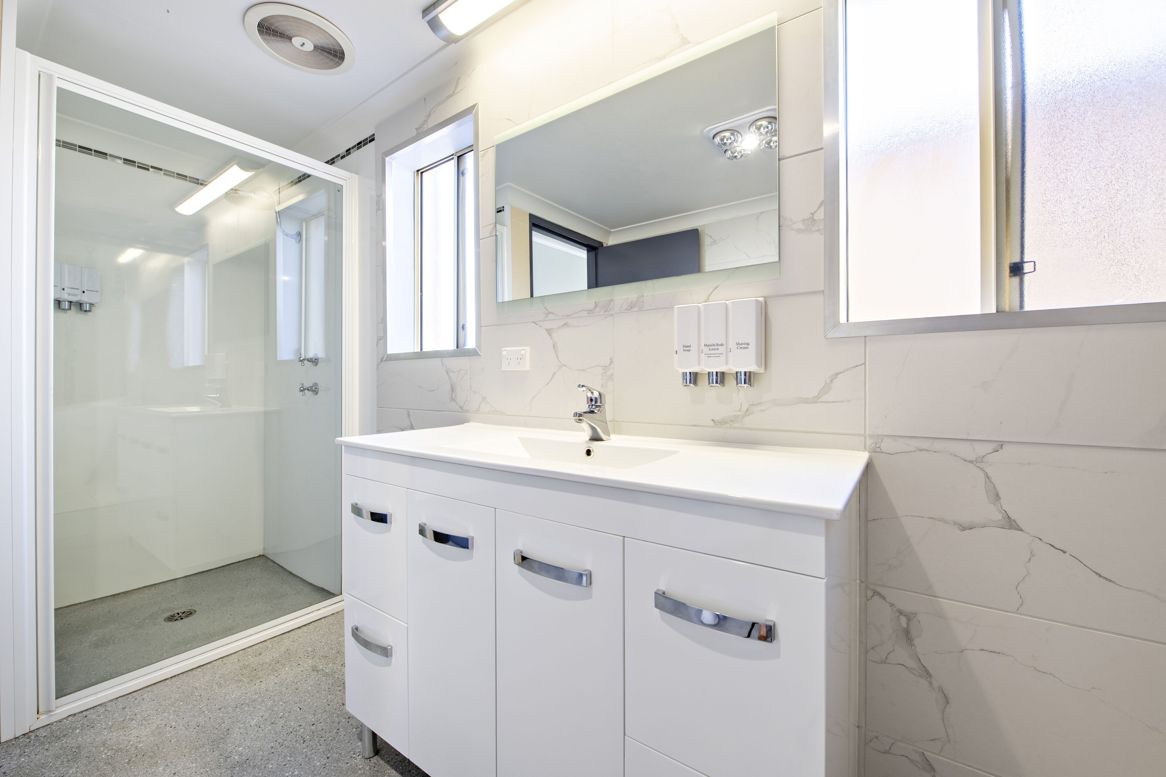 A modern bathroom with a glass-enclosed shower, a white vanity with a marble countertop, and a large mirror above the sink.
