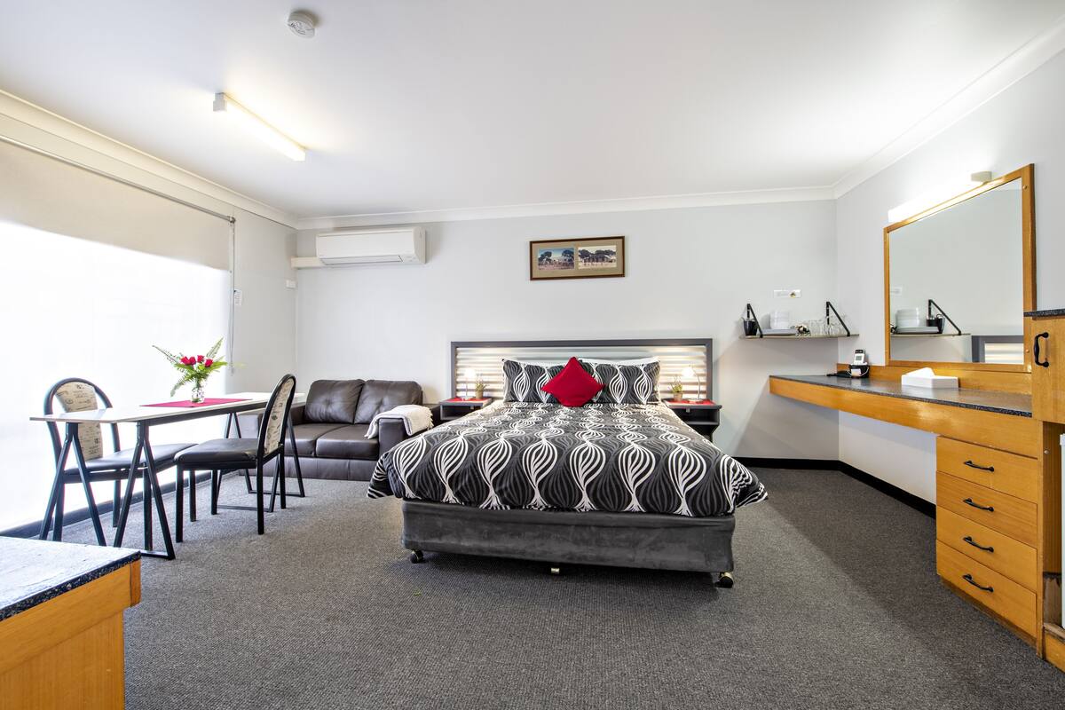 A hotel room with a bed, a desk, a chair, a sofa, a dresser, and a mirror.