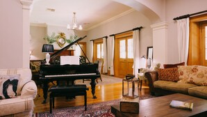 A spacious living room with a grand piano, a sofa, a coffee table, and a chandelier. - Flowerdale Estate (Strath Creek)