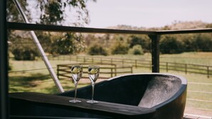 A balcony with two glasses of wine, a wooden bench, and a view of a fenced field and trees. - Flowerdale Estate (Strath Creek)