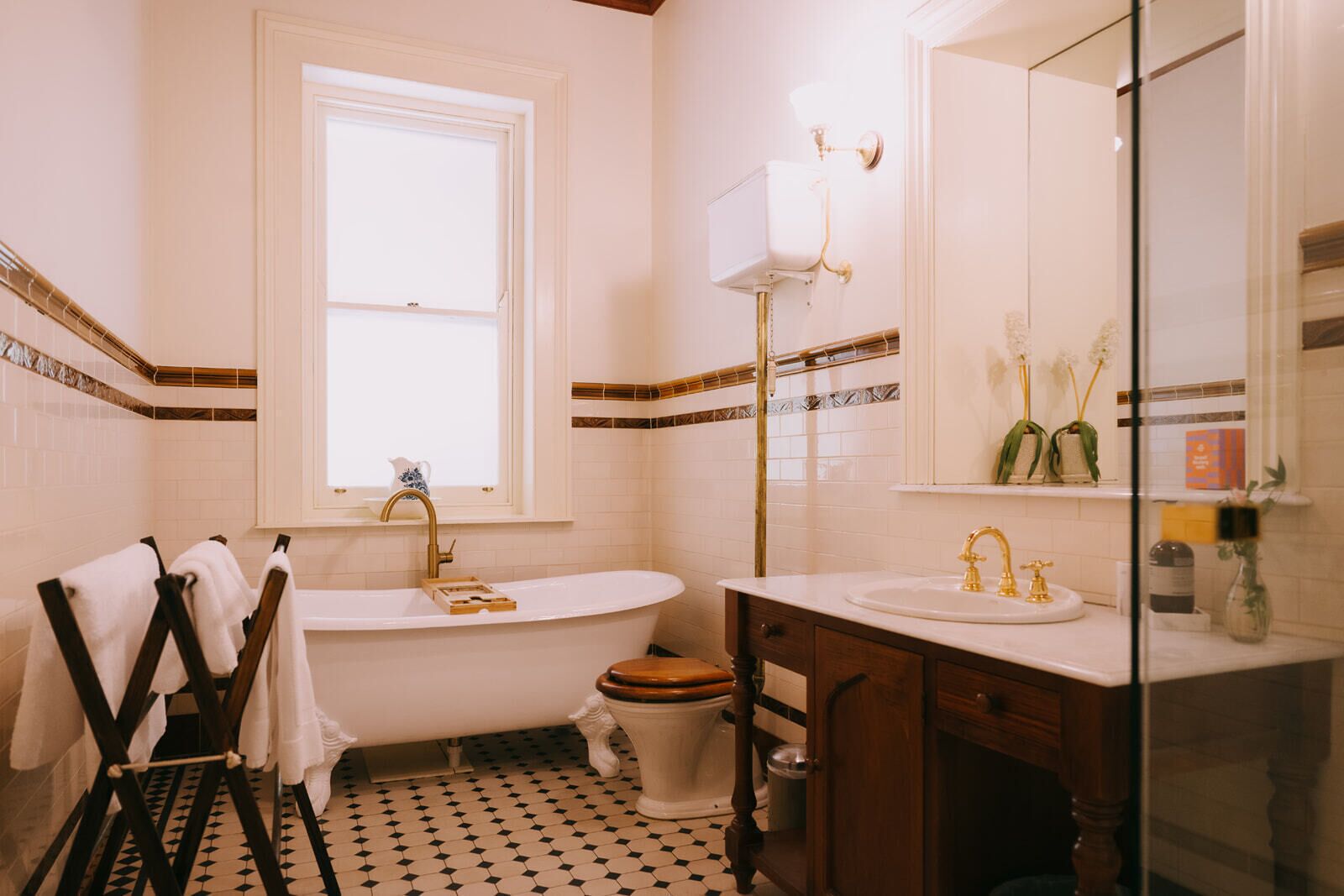 Un baño con bañera, lavamanos e inodoro. Hay una ventana sobre la bañera y un espejo sobre el lavamanos.