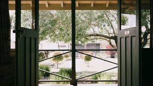 A view through a wooden door with a metal gate, leading to a garden with various plants and a tree. - Flowerdale Estate (Strath Creek)