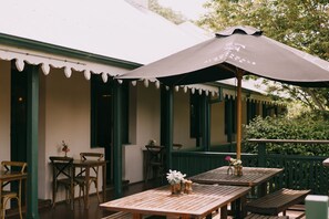 An outdoor patio with wooden tables and chairs, a large umbrella, and a green fence. - Flowerdale Estate (Strath Creek)