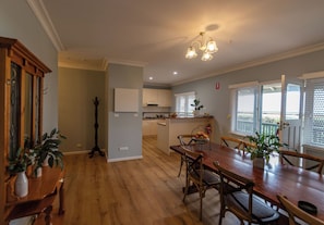 Un comedor espacioso con una mesa y sillas de madera, una cocina al fondo y un candelabro en el techo.