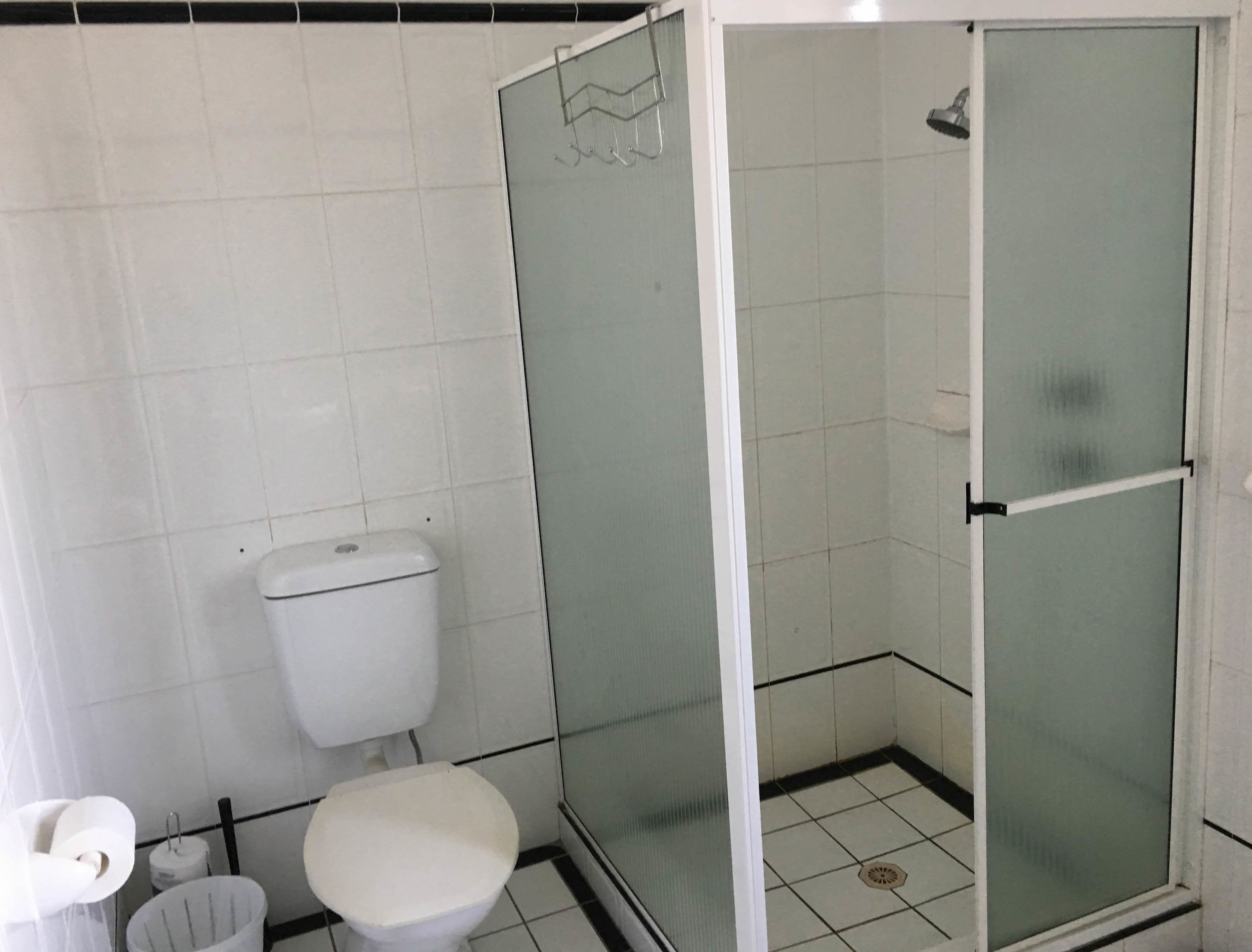 A small, tiled bathroom with a toilet, a shower enclosure, and a toilet paper holder.