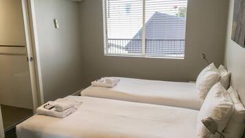 A hotel room with two beds, a window with blinds, a door, and a wall-mounted air conditioner.