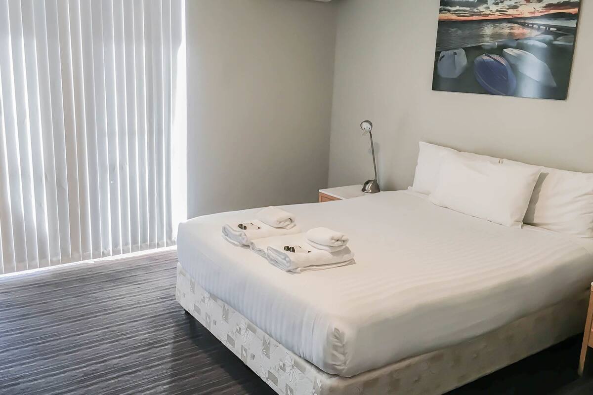 A hotel room with a bed, a nightstand, a lamp, and a painting on the wall.