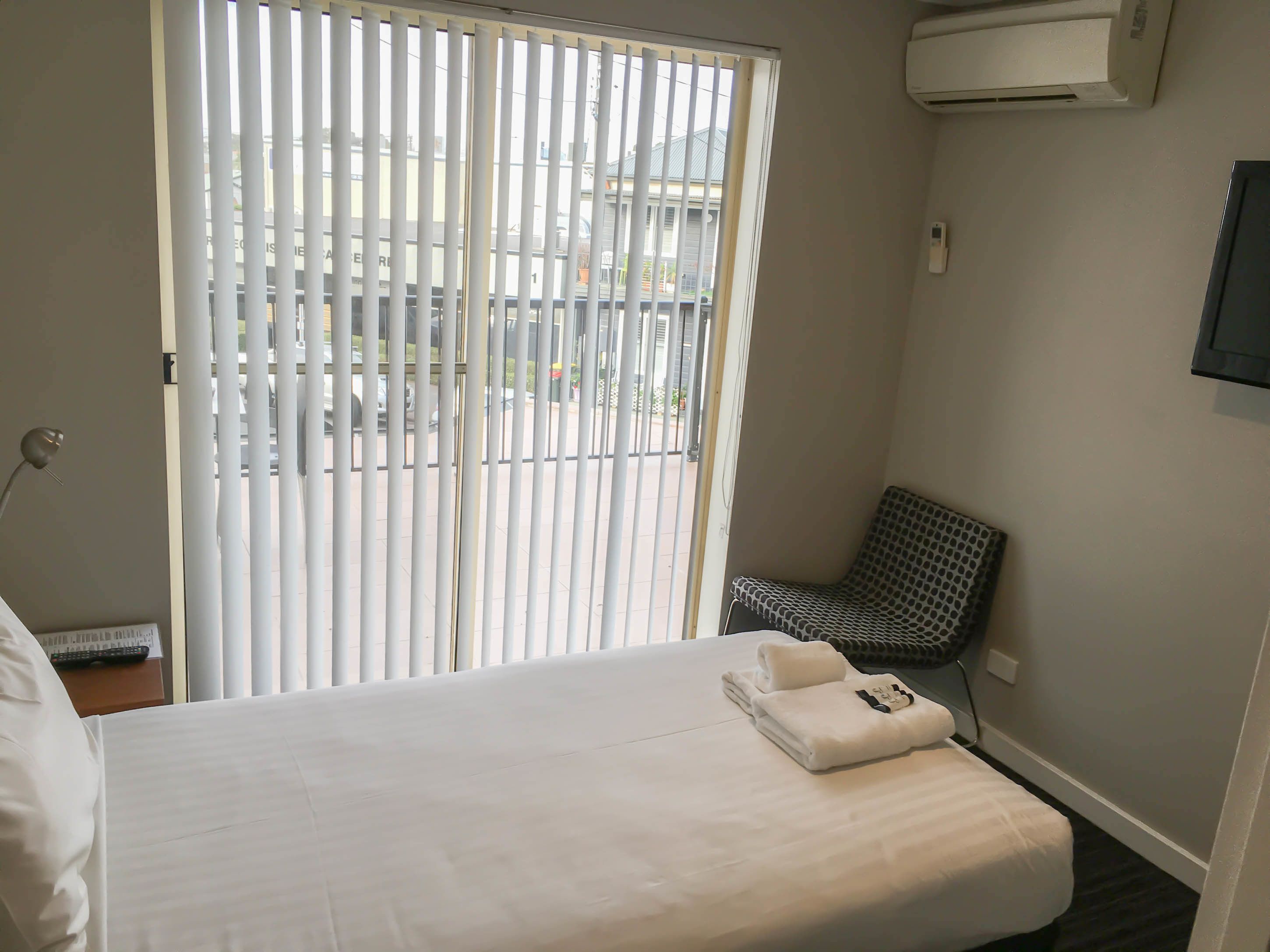 Une chambre d’hôtel avec un lit, une chaise et une fenêtre avec des stores.