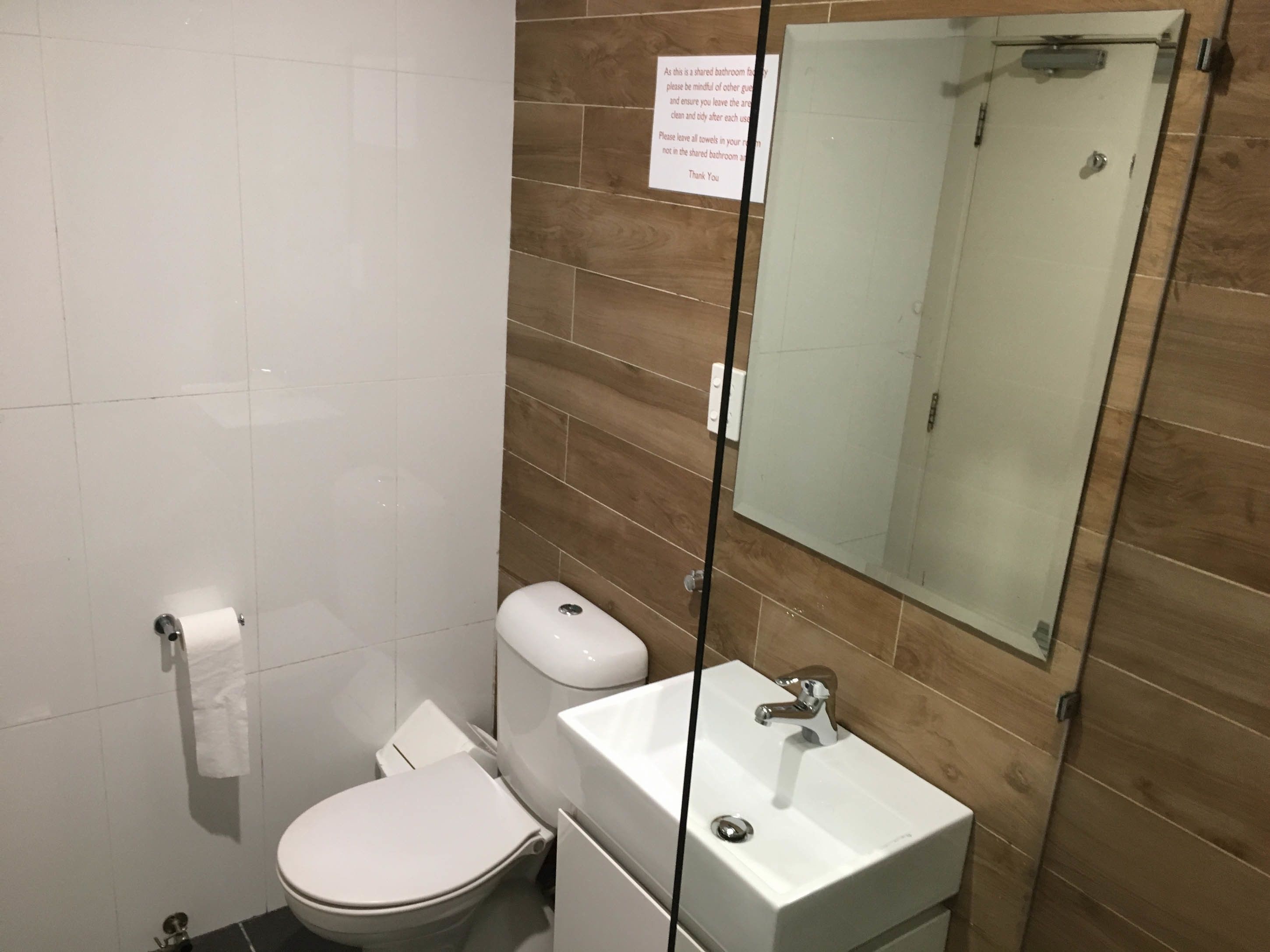 A bathroom with a toilet, sink, and mirror. There is a sign on the wall.
