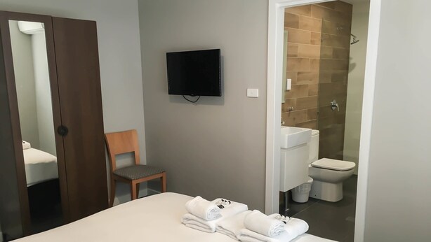 A hotel room with a bed, a chair, a TV mounted on the wall, and a bathroom visible through an open door. - The Premier Hotel (Broadmeadow)
