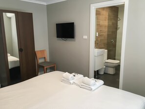 Une chambre d’hôtel avec un lit, une chaise, un téléviseur fixé au mur et une salle de bain visible à travers une porte ouverte.