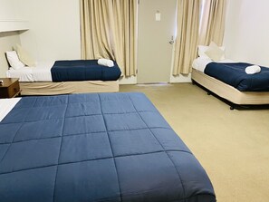 A hotel room with two single beds, a large bed, a nightstand, and a door with curtains. - Millers Cottage Motel (Wangaratta)