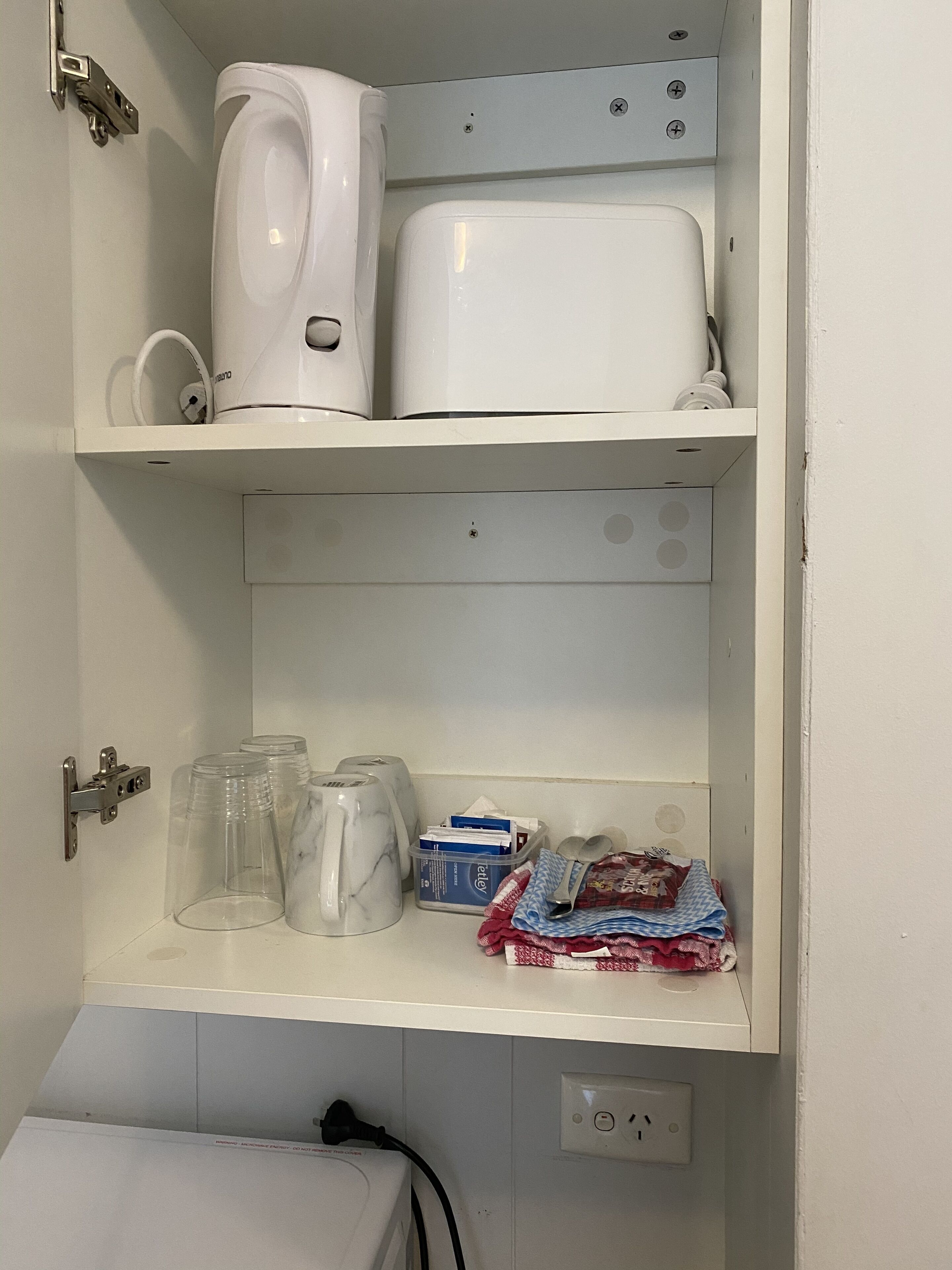 A white bathroom with a toilet, a sink, and a mirror. There are toiletries on the counter, including a toothbrush, toothpaste, and a towel.