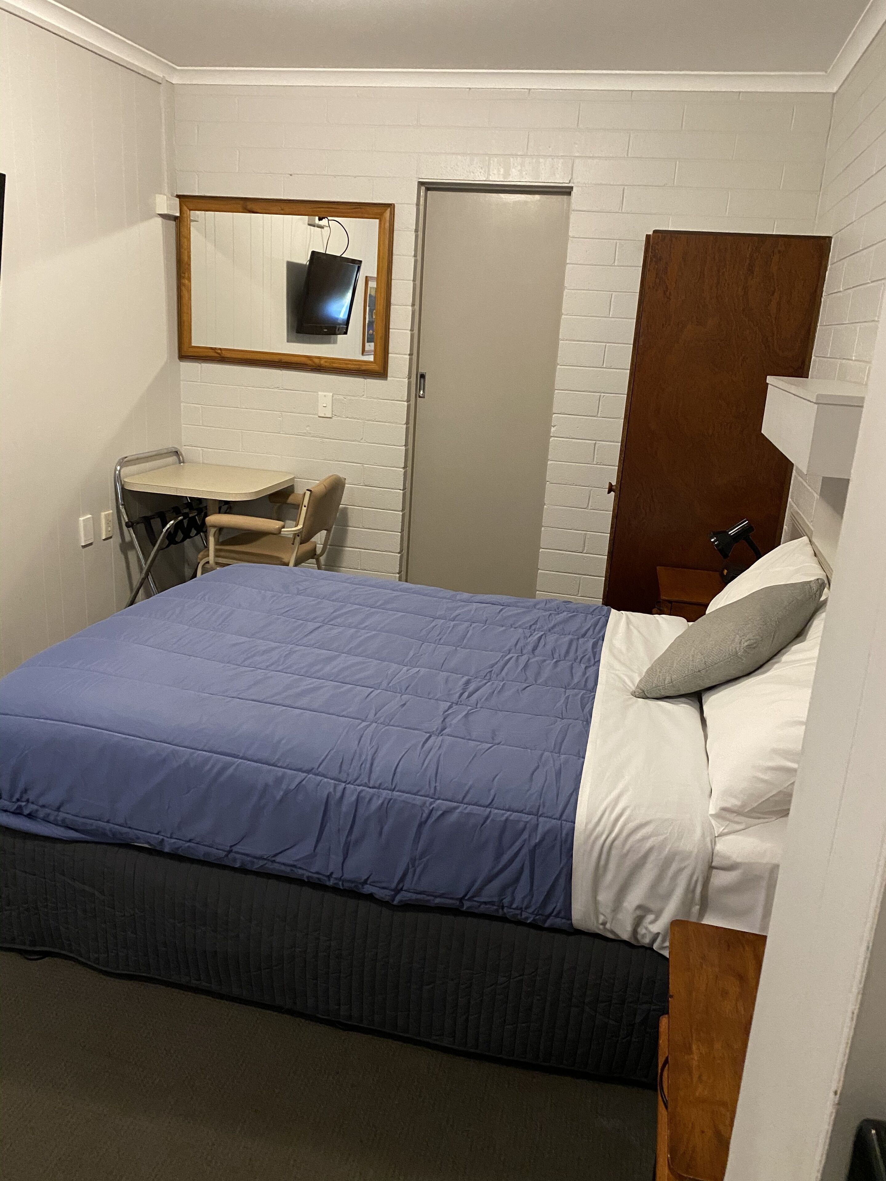 A bedroom with a bed, a desk, a chair, a mirror, and a door.