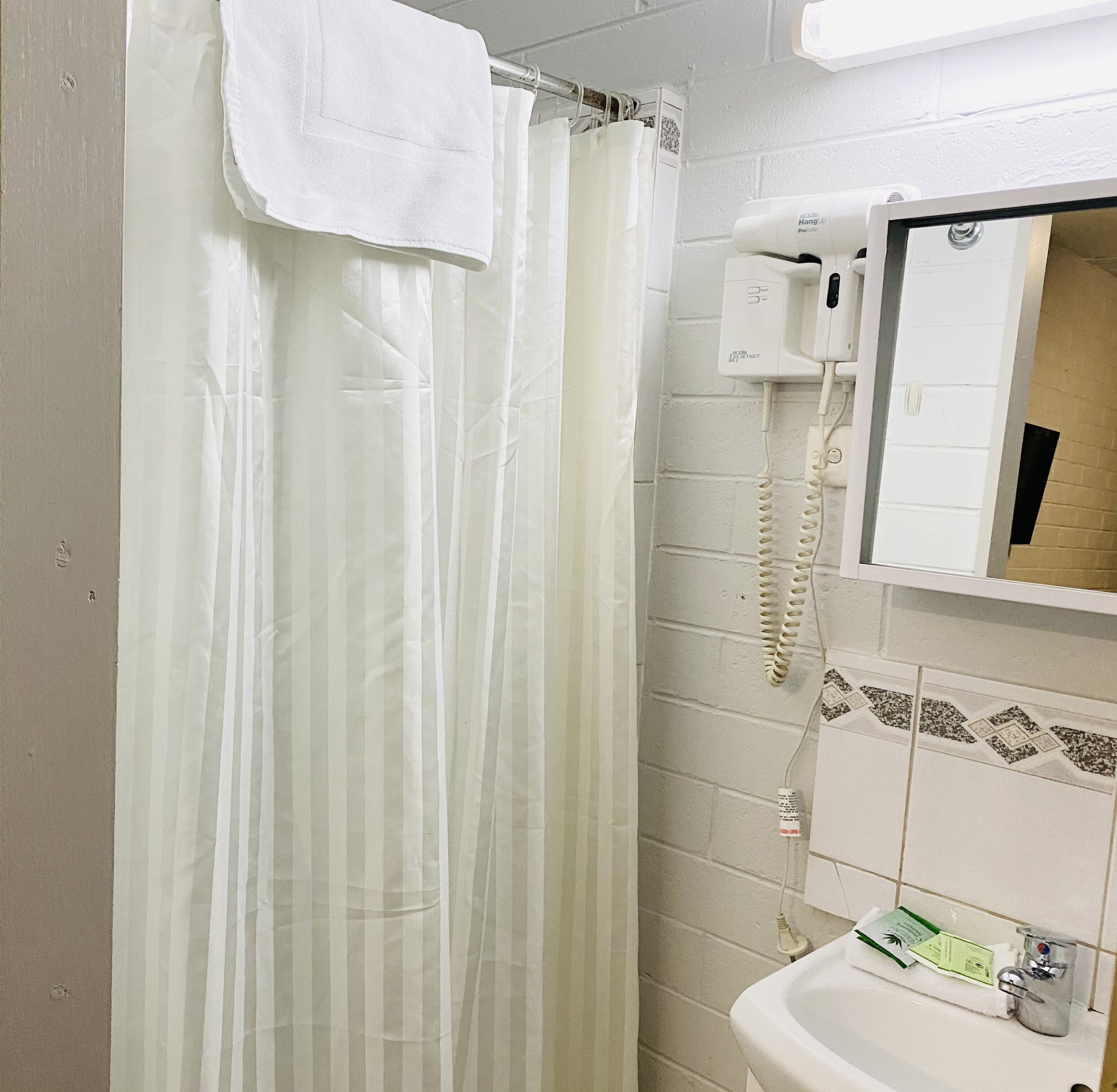 A bathroom with a shower curtain, a hanging telephone, a sink, and a mirror.
