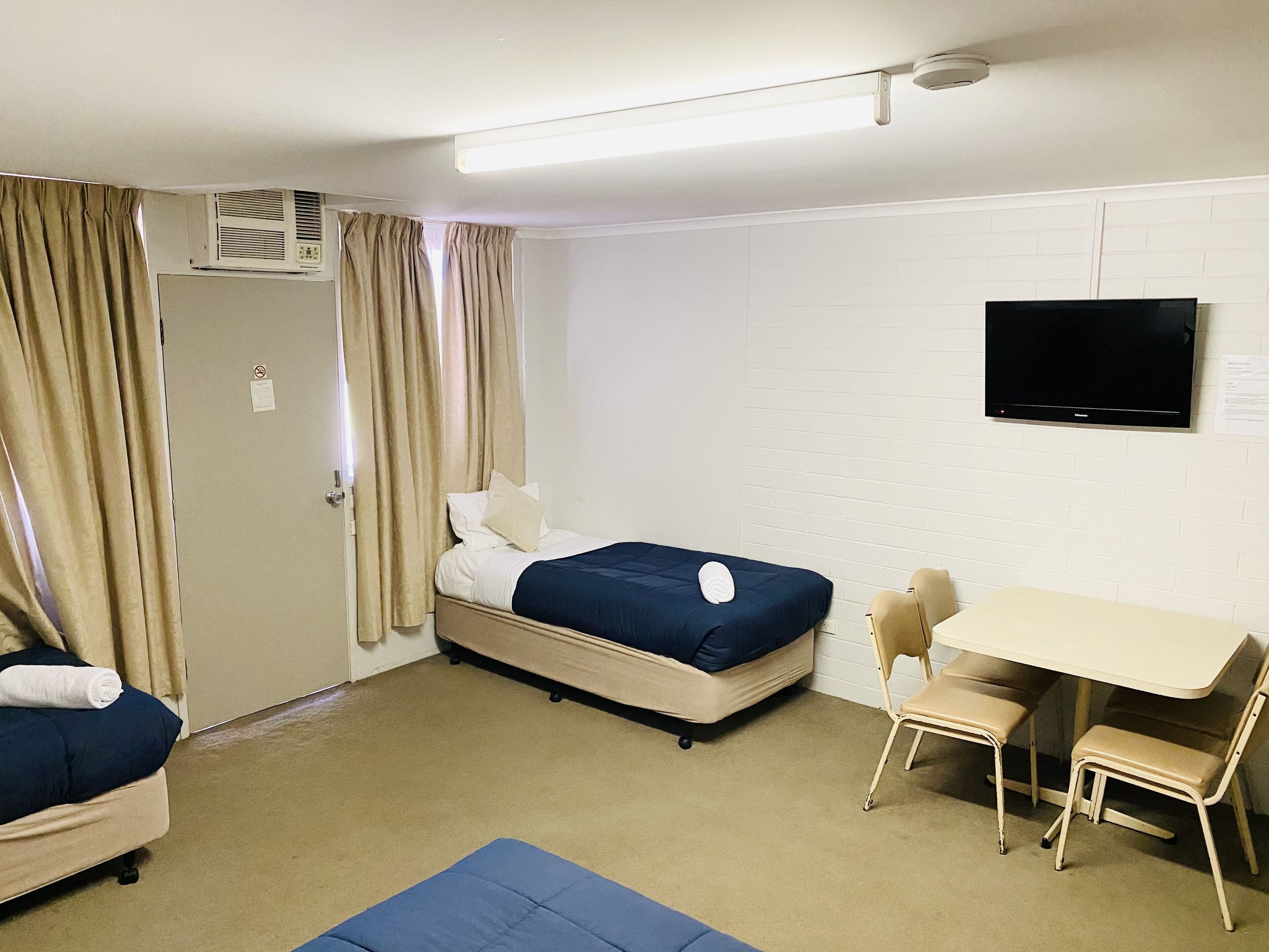 Quarto de hotel com uma cama, uma mesa, duas cadeiras, uma televisão e cortinas.