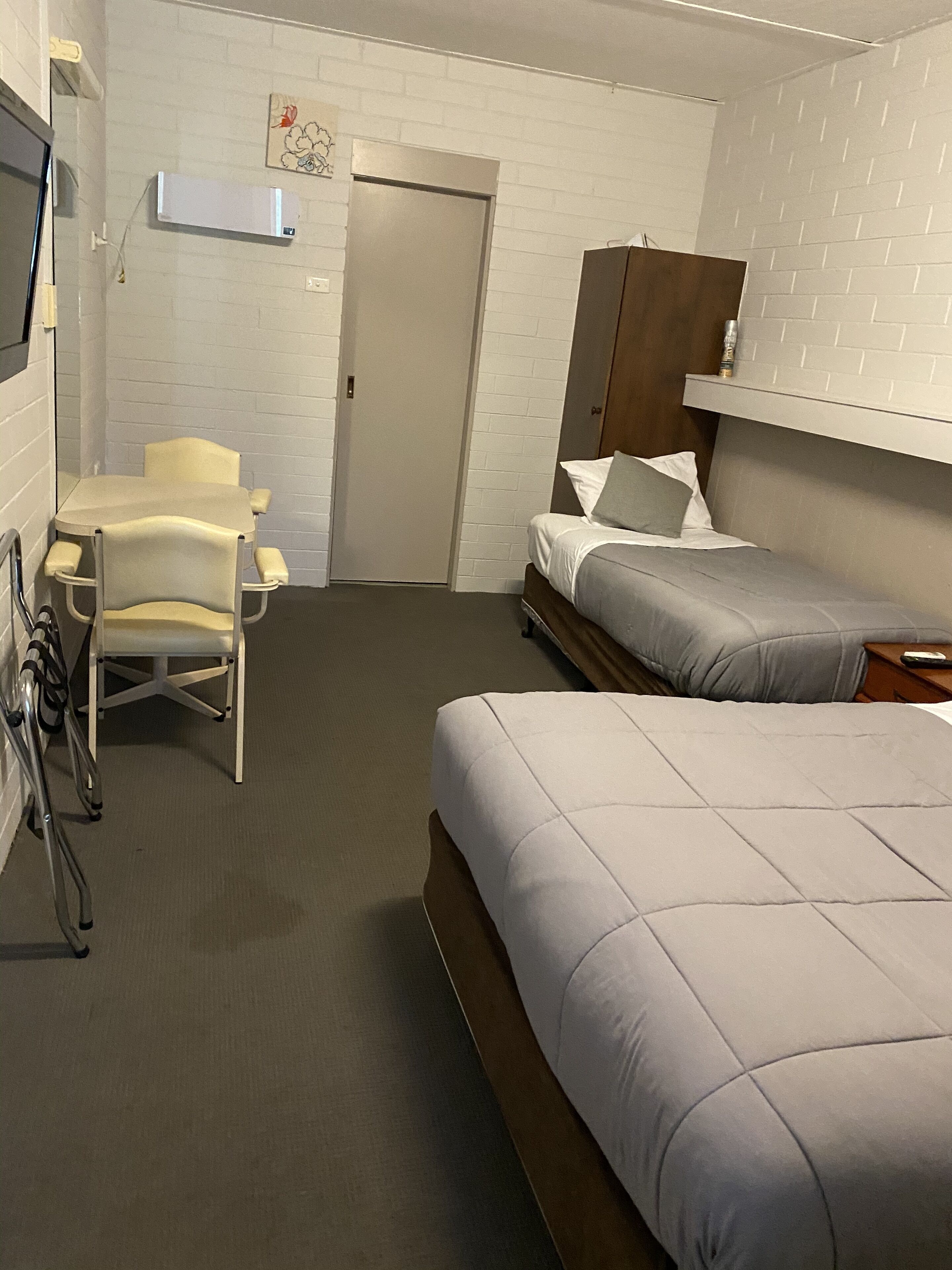 A hotel room with a bed, a desk with a chair, a door, and a wall-mounted TV.