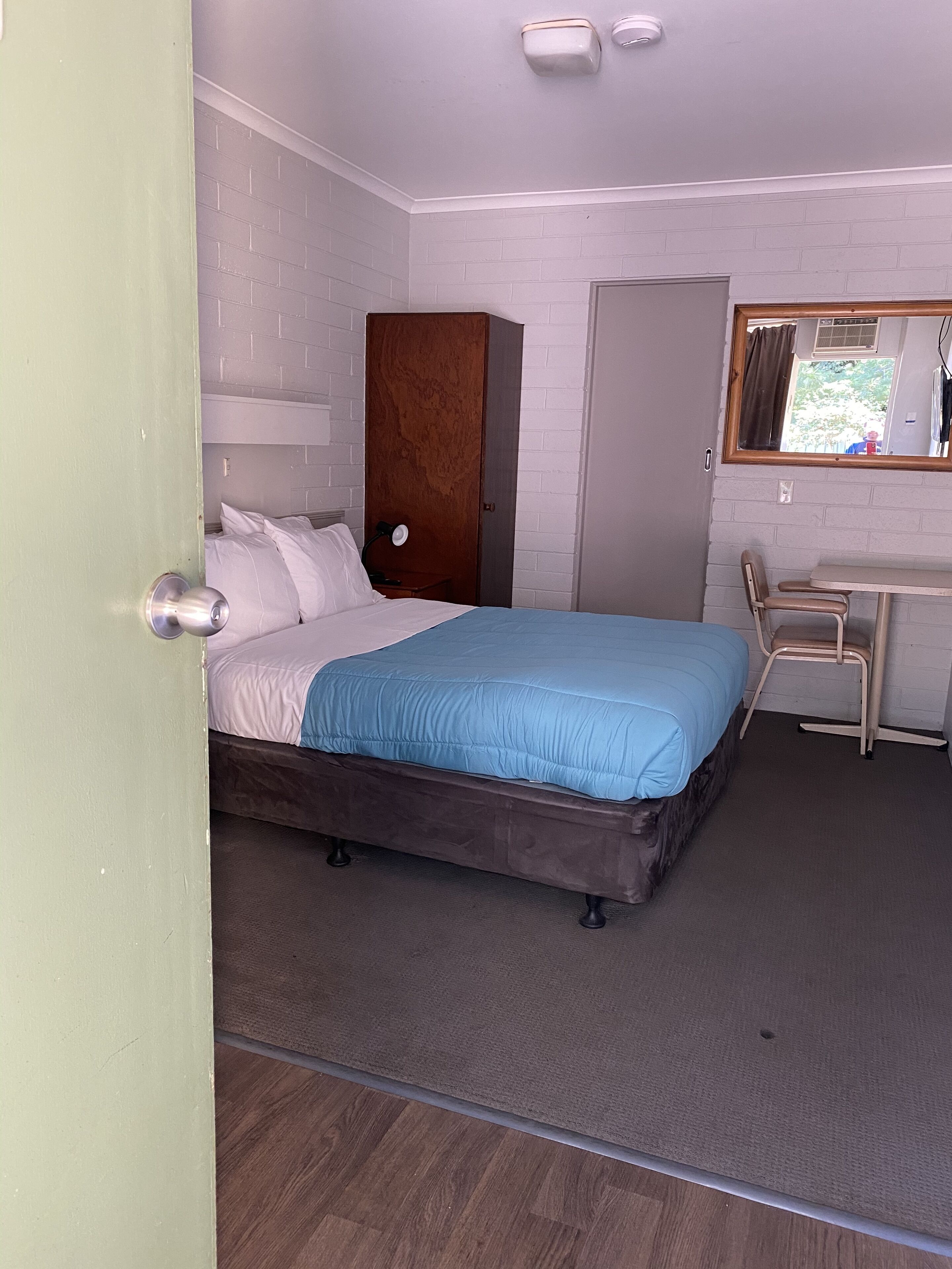 A room with a bed, a desk, a chair, a wardrobe, and a mirror.