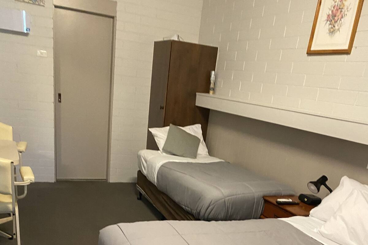 Una habitación de hotel con dos camas, un armario de madera, un escritorio y una silla.