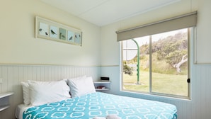 Une chambre à coucher avec un lit, une fenêtre donnant sur un paysage verdoyant, une étagère remplie de livres et des tableaux encadrés accrochés au mur.