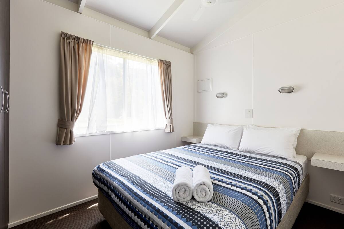 Una habitación de hotel con una cama grande, una mesita de noche, una ventana con cortinas y un ventilador de techo.