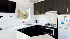Une cuisine moderne avec des meubles noirs, un plan de travail blanc, un four à micro-ondes encastré, une cuisinière à gaz et un téléviseur à écran plat fixé au-dessus de l’évier.