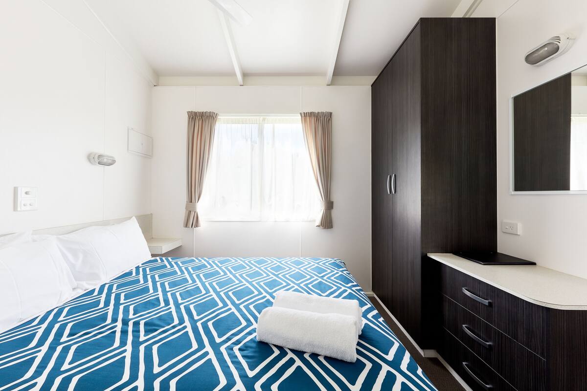 Habitación de hotel con cama, mesita de noche, armario y ventana con cortinas.