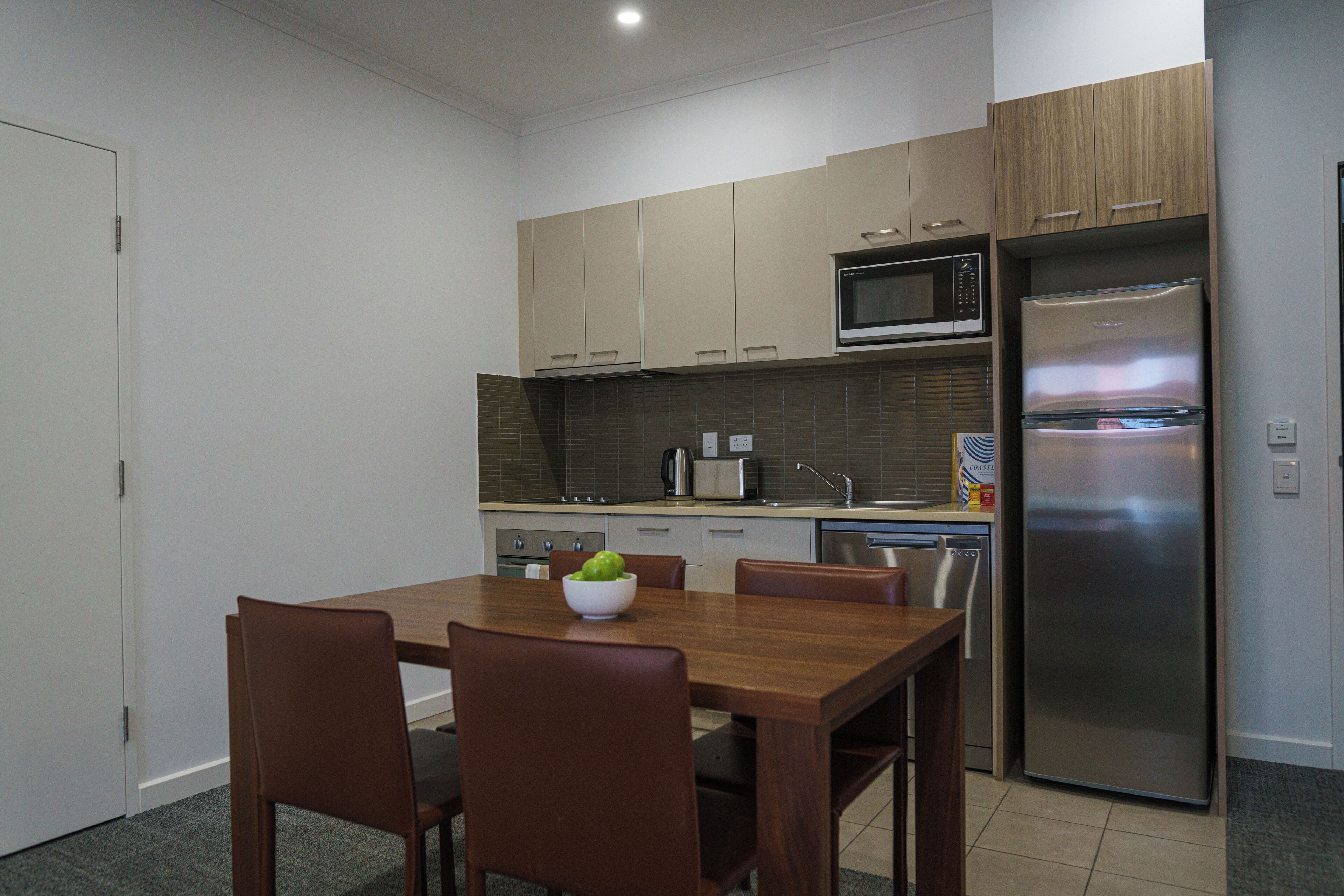 Una cocina moderna con armarios de madera, un refrigerador de acero inoxidable, un microondas y una mesa de comedor con sillas.