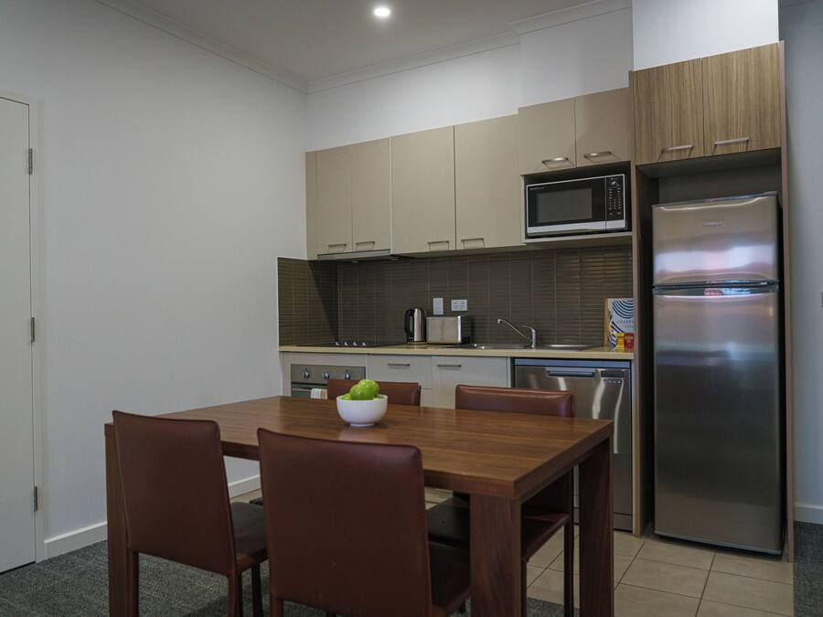 Una cocina moderna con armarios de madera, un refrigerador de acero inoxidable, un microondas y una mesa de comedor con sillas.