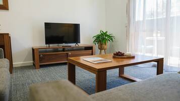 Una sala de estar con un mueble bajo para televisión de madera, un televisor de pantalla plana, una mesa de centro de madera con una revista, una planta y una bandeja de frutas.