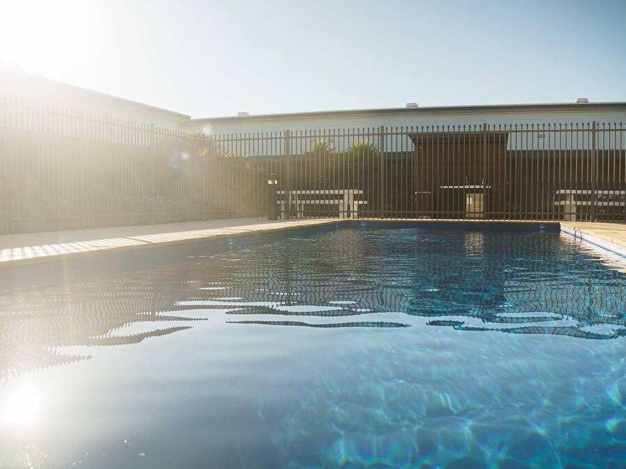 Una piscina con superficie de agua cristalina, rodeada por una cerca y un edificio al fondo.