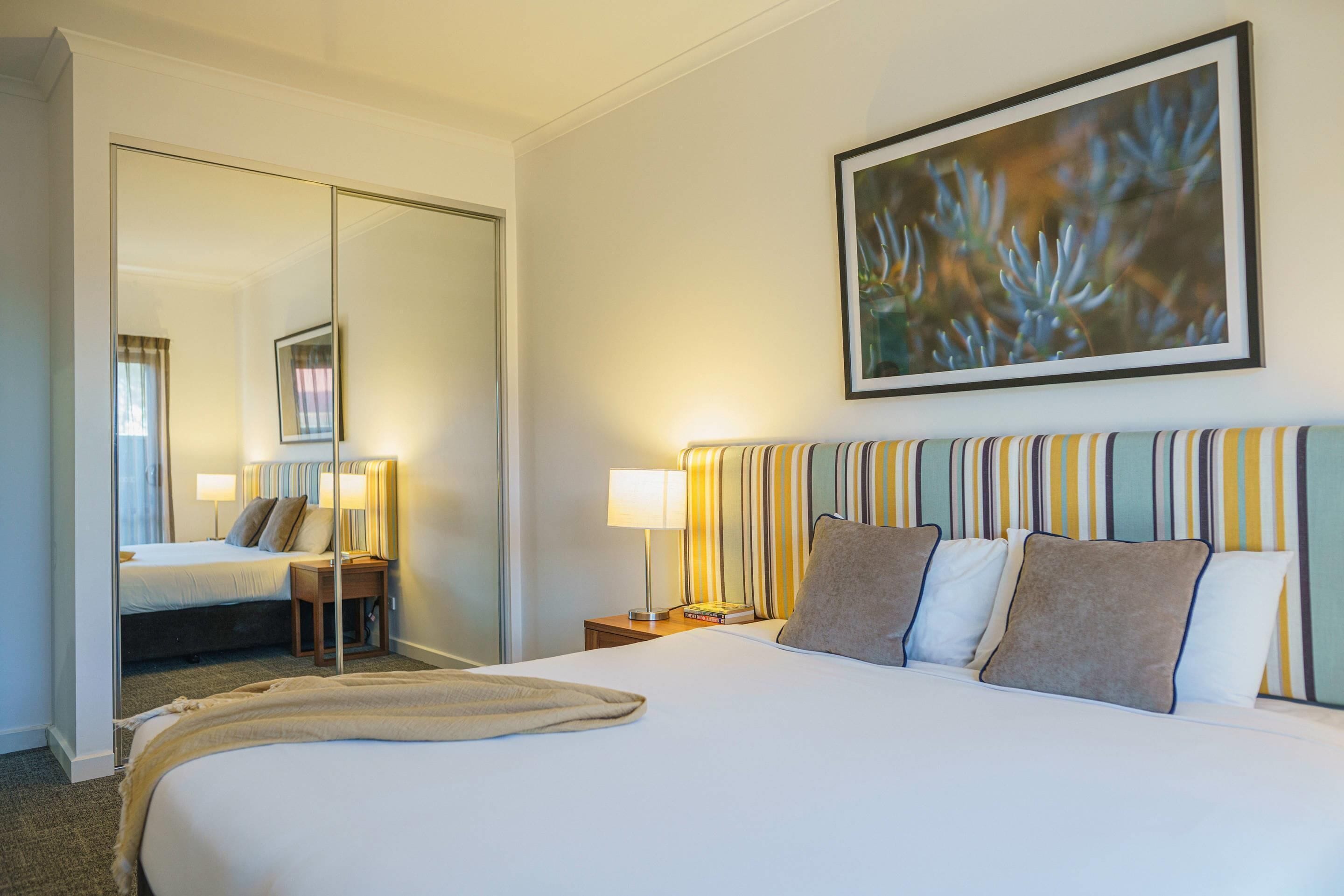 Una habitación de hotel con cama, mesita de noche, lámpara y espejo.