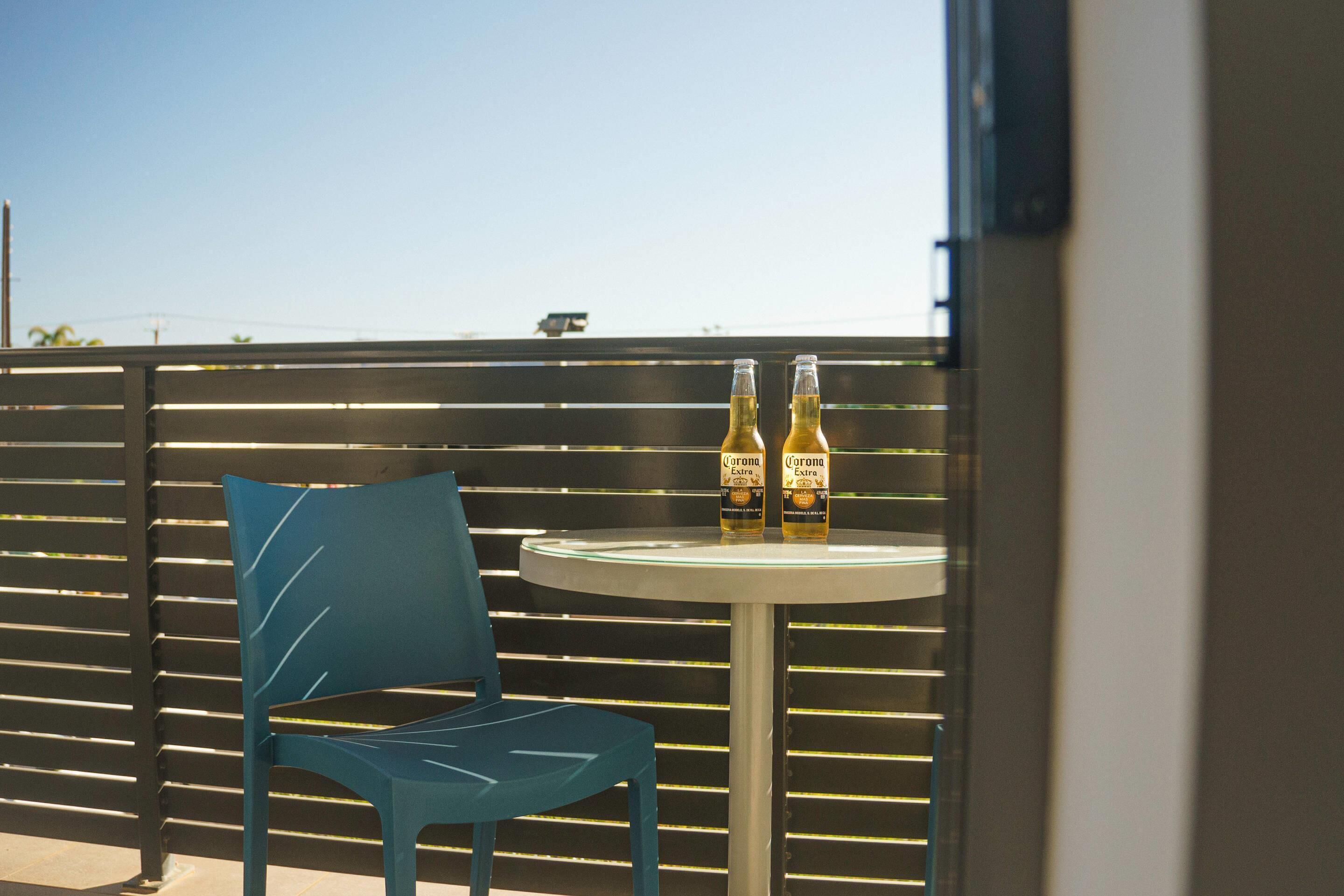 A balcony with a blue chair and a small round table holding two bottles of Corona Extra beer.
