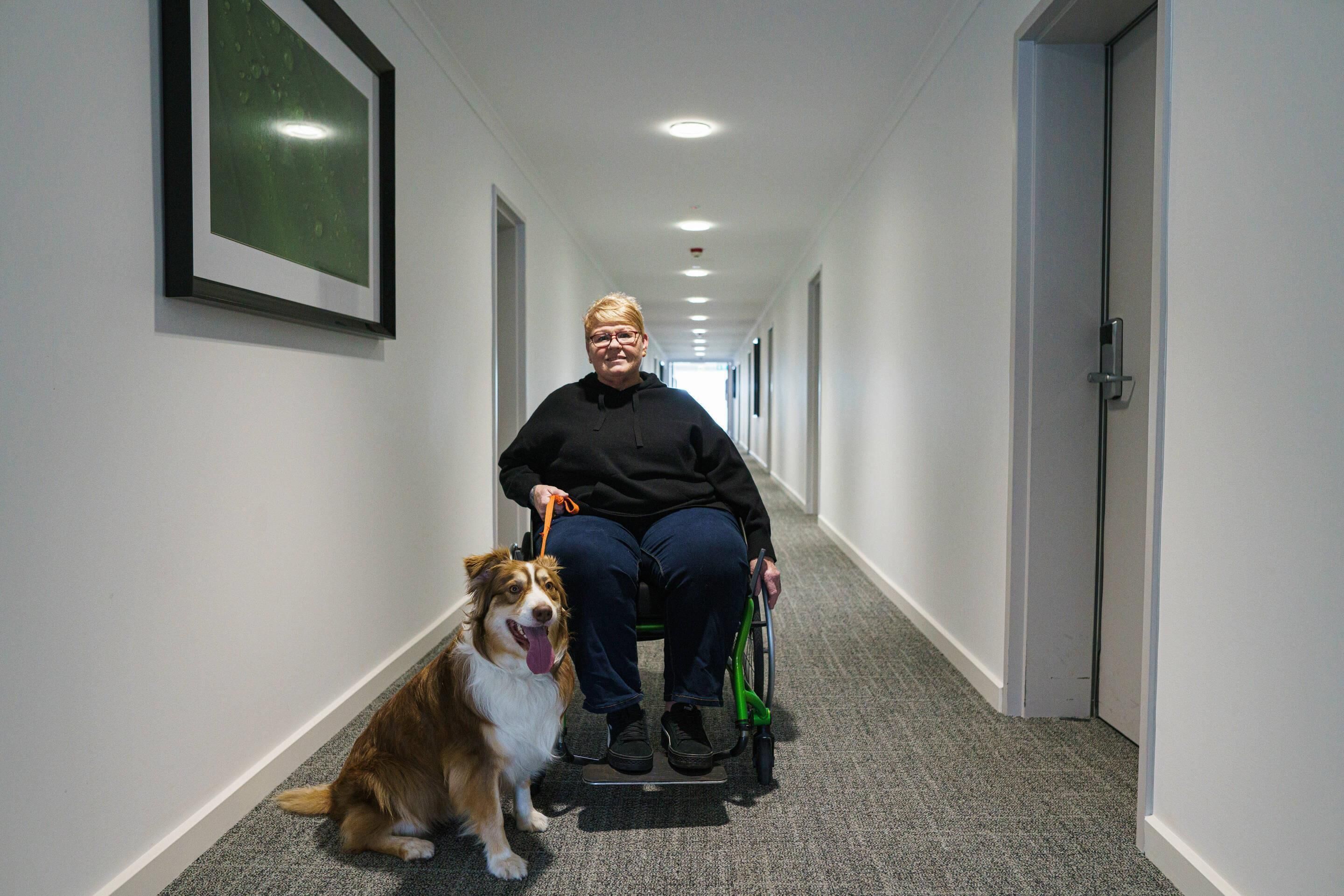 Een persoon in een rolstoel in een gang met een hond.