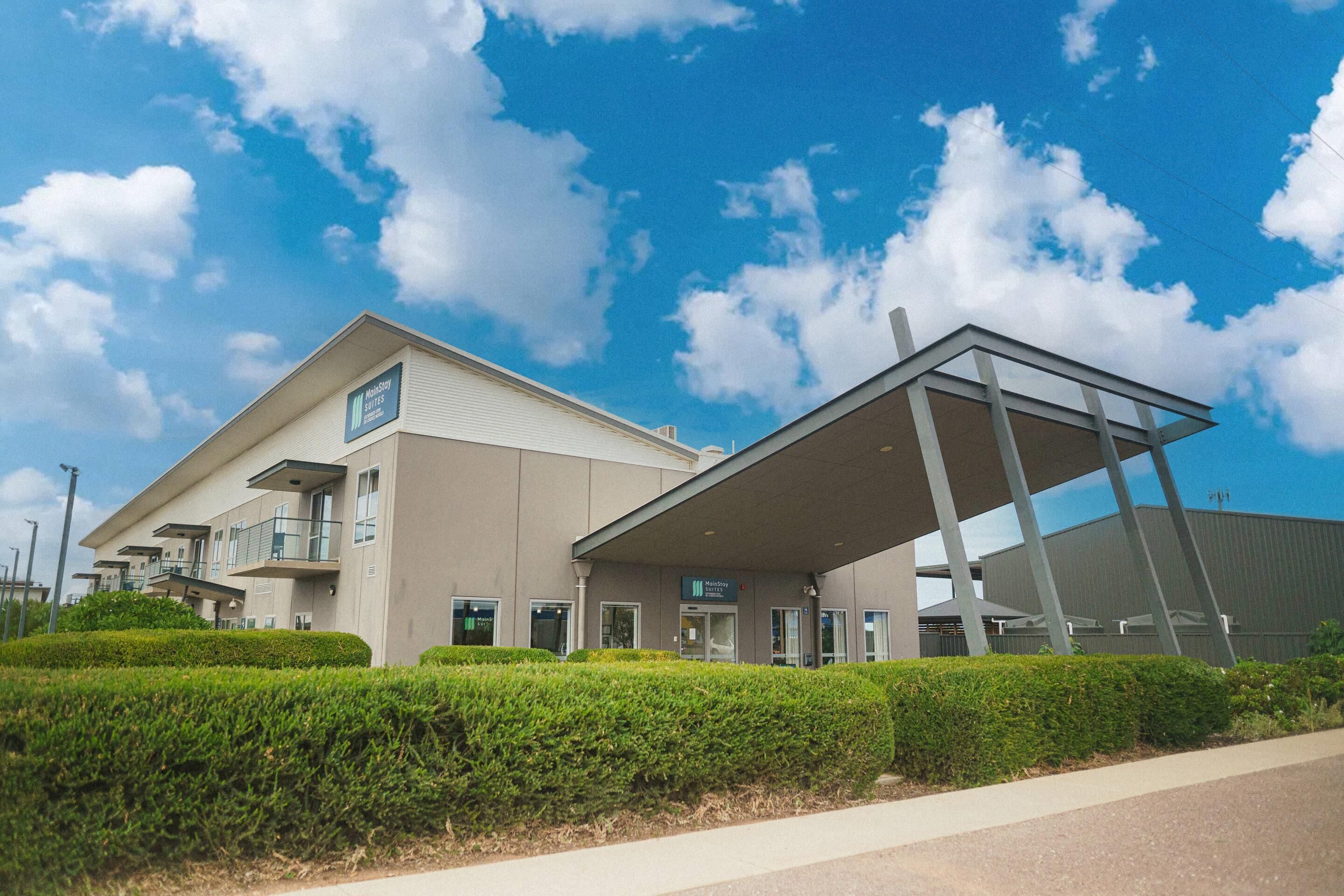 A MainStay Suites hotel with a modern design, featuring a flat roof, large windows, and a covered outdoor area.