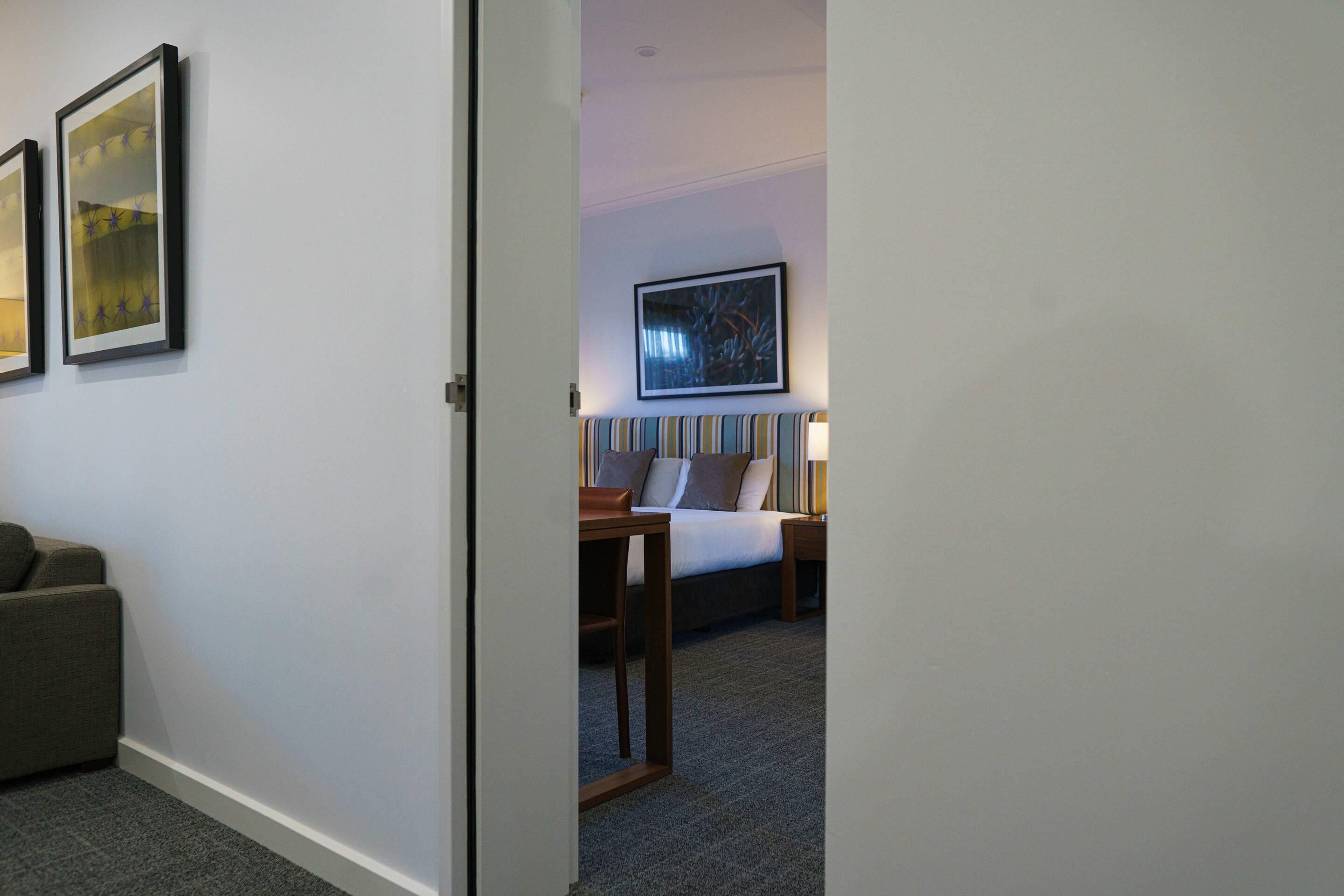 A hotel room with a bed, bedside table, lamp, and a framed picture on the wall.