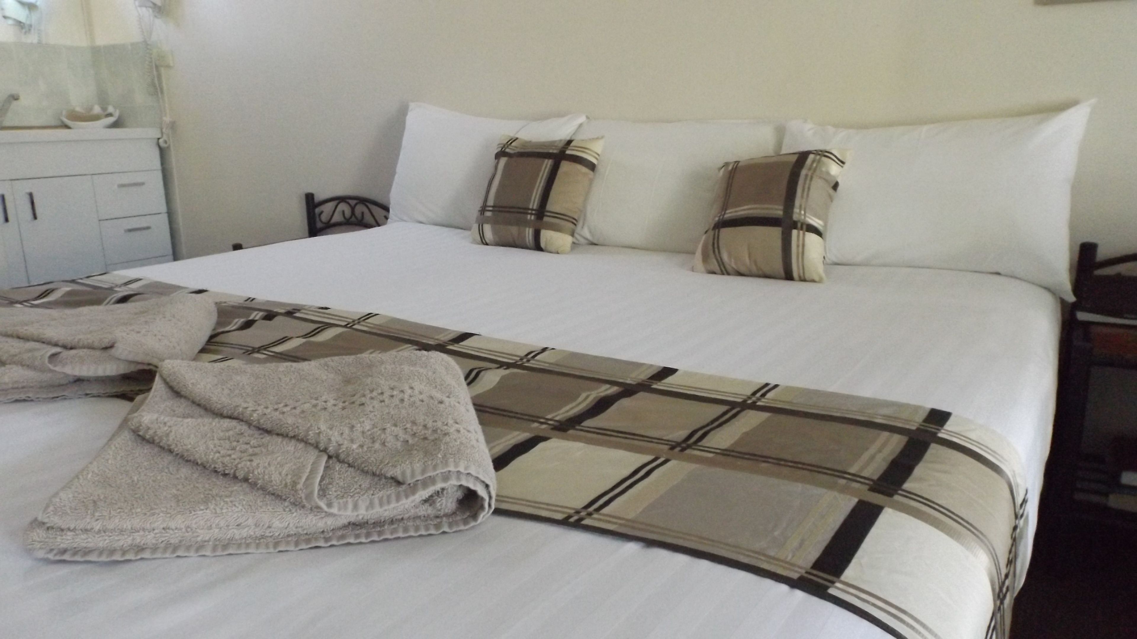 A neatly made bed with a plaid bedspread, a folded towel, and two pillows with a striped pattern.