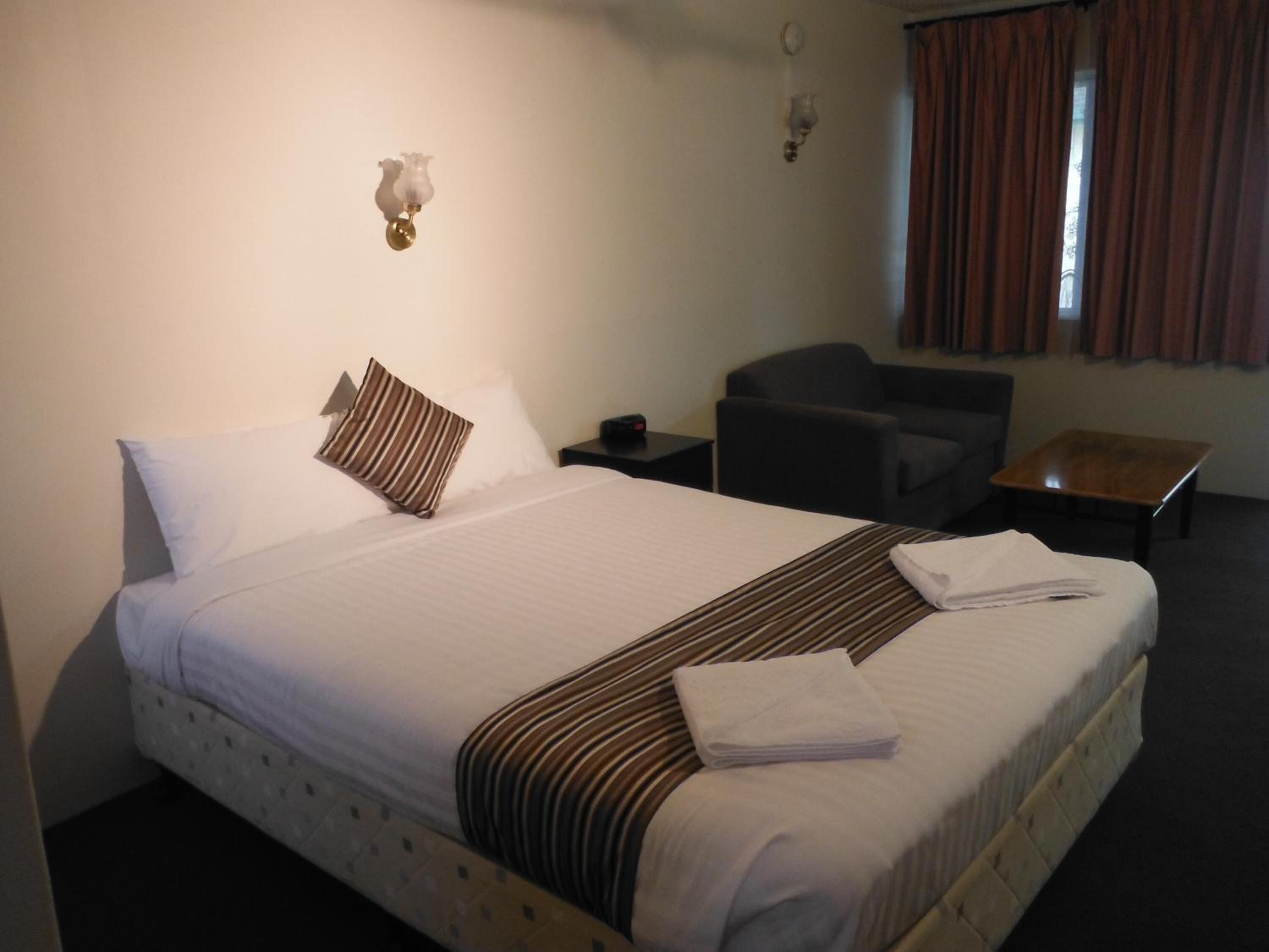Une chambre d’hôtel avec un lit, une chaise, une petite table et une fenêtre avec des rideaux.