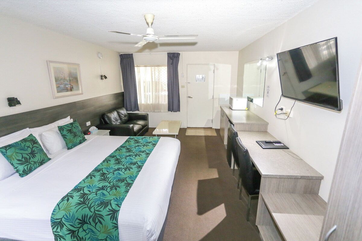 Habitación de hotel con cama, escritorio, televisión, ventilador de techo y puerta.